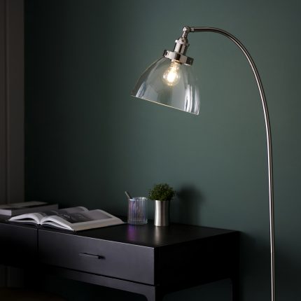 A top half view of the Ferri Floor Lamp in Polished Nickel with a clear glass shade, positioned next to a desk.