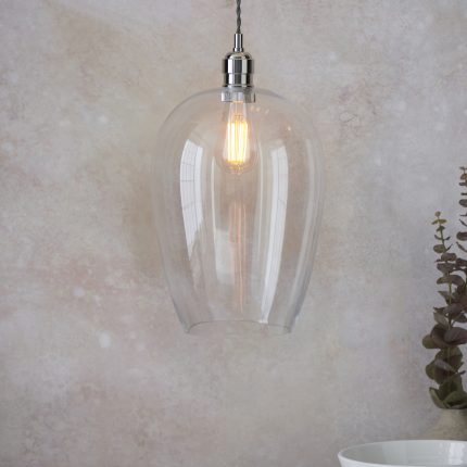 Close-up of the Nova Large Glass Pendant Light in Nickel, showcasing its transparent glass against a contrasting stone wall background.
