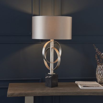 Oratio Table Lamp with silver leaf hoops and mink drum shade positioned on a wooden table, viewed from eye level at a distance.