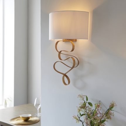 Side view of the Ludu Wall Lamp with gold finish and ivory lampshade, 1 light, installed on a wall next to a dining room entrance.