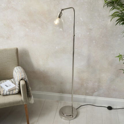 Freddo floor lamp with polished nickel frame and clear glass shade positioned beside reading chair.