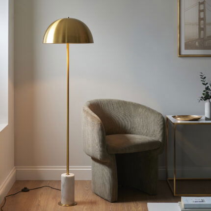 Charan floor lamp with brass dome shade and white marble base positioned beside reading chair.