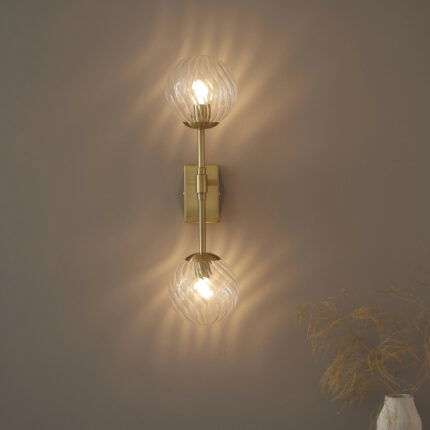 Front view of Deo wall light showing two twisted glass shades and brass frame at eye level.