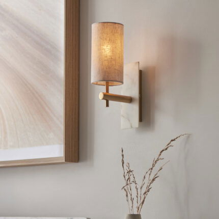 Low angle right side view of wall lamp with two cylinder shades on brass arms extending from white marble mount.