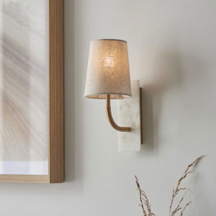 Wall lamp with brass curved arm, marble base and tapered shade viewed upward from right side.