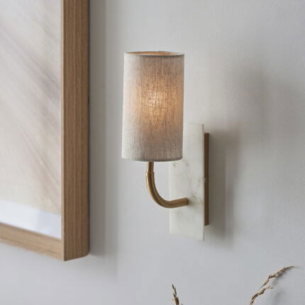Eye level right side view of wall light with curved brass arm extending from marble mount with natural fabric shade.