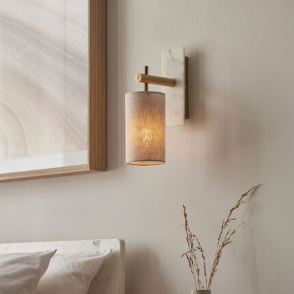 Cylinder wall lamp with brass arms and marble mount installed beside bed with white bedding.