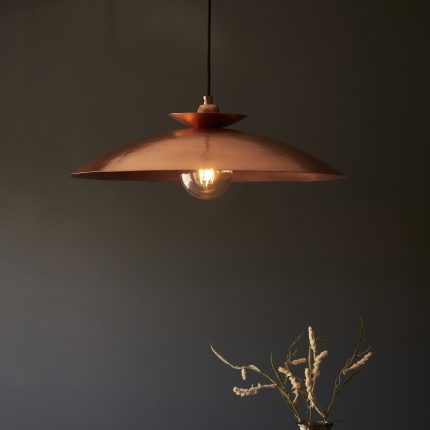 Close up of hammered copper pendant light shade texture against navy blue background.