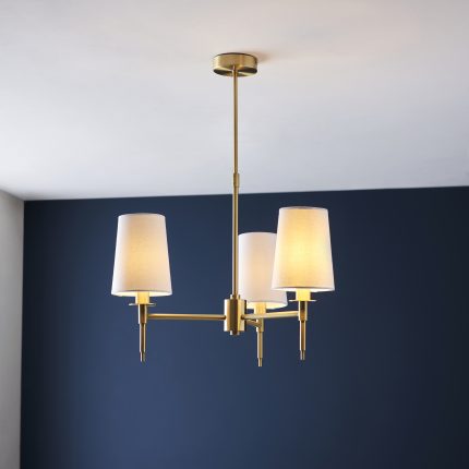 Zoomed-in view of the Lilt Rod Chandelier in brass with 3 arms and white shades, 55cm, set against a navy wall.