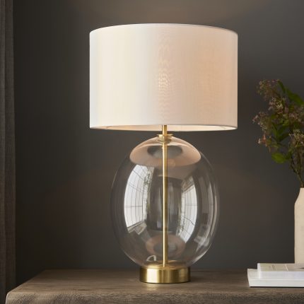 Zoomed-in front-facing view of the Vial Touch Table Lamp in brass with oval glass and white shade, light bulb switched on.