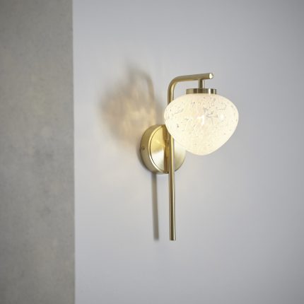 Ember Brass Wall Light With Glass Shade on an off-white wall, lit with a warm white light bulb.