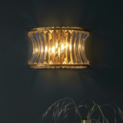 Front view of the Ares Wall Light in brushed brass with crystal glass and two lights against a dark wall.