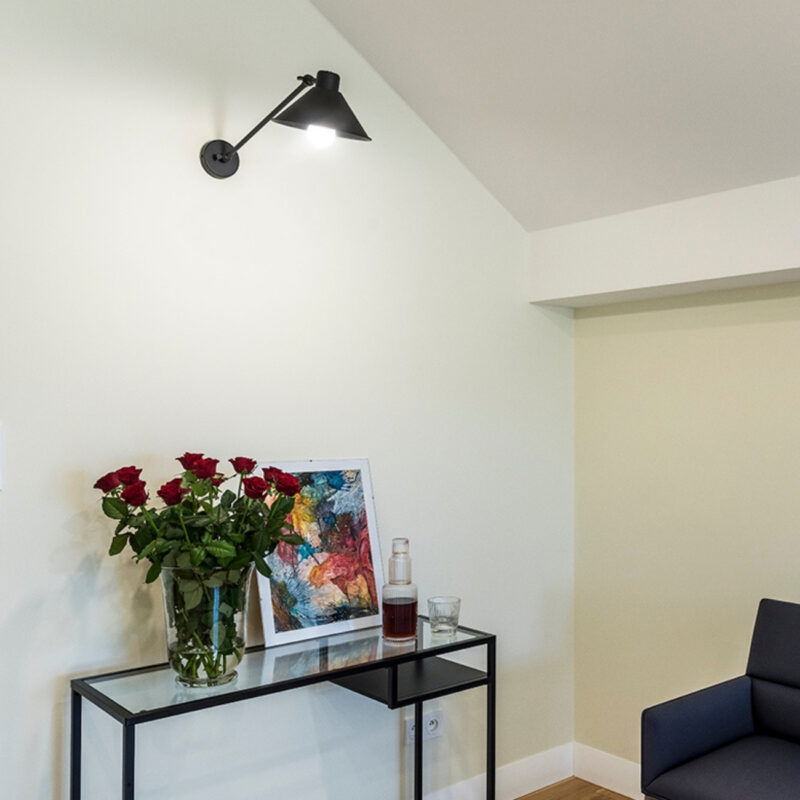 Black Alea wall lamp on wall with adjustable arm and cone shade.